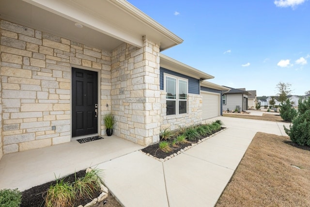 view of exterior entry featuring stone siding, an attached garage, and driveway