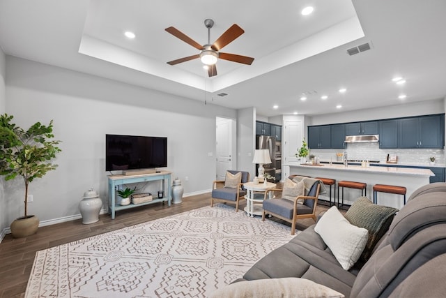 living room featuring a raised ceiling, dark hardwood / wood-style floors, and ceiling fan