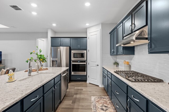 kitchen with tasteful backsplash, wood-type flooring, sink, stainless steel appliances, and light stone countertops