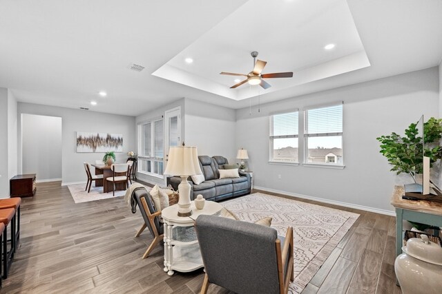 living room featuring light hardwood / wood-style flooring, a raised ceiling, and ceiling fan