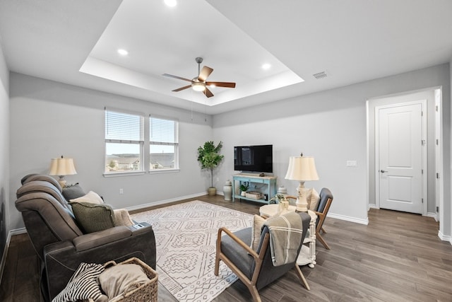 living room with baseboards, visible vents, a raised ceiling, ceiling fan, and wood finished floors