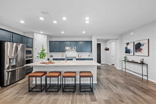 kitchen featuring light stone countertops, appliances with stainless steel finishes, a center island with sink, and a kitchen breakfast bar