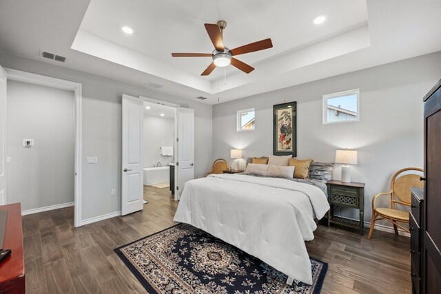 bedroom featuring a raised ceiling, ceiling fan, connected bathroom, and dark hardwood / wood-style flooring