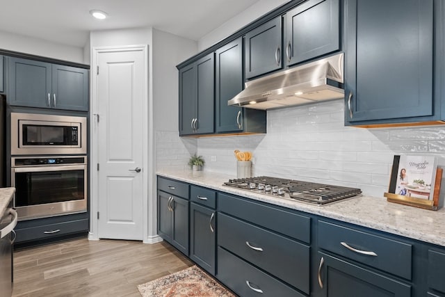 kitchen with blue cabinetry, appliances with stainless steel finishes, tasteful backsplash, light stone countertops, and light wood-type flooring