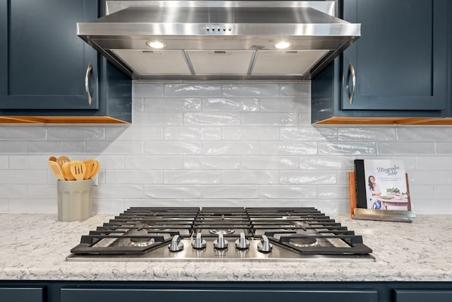 kitchen featuring blue cabinetry, tasteful backsplash, extractor fan, light stone countertops, and stainless steel gas cooktop