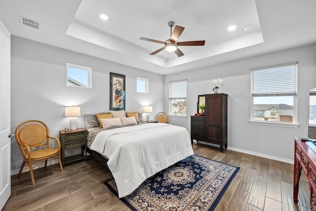 bedroom with baseboards, visible vents, a raised ceiling, and wood finished floors