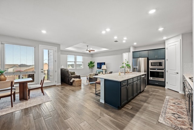 kitchen featuring stainless steel appliances, an island with sink, wood-type flooring, and a breakfast bar