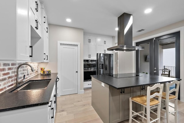 kitchen with sink, white cabinetry, island range hood, appliances with stainless steel finishes, and backsplash