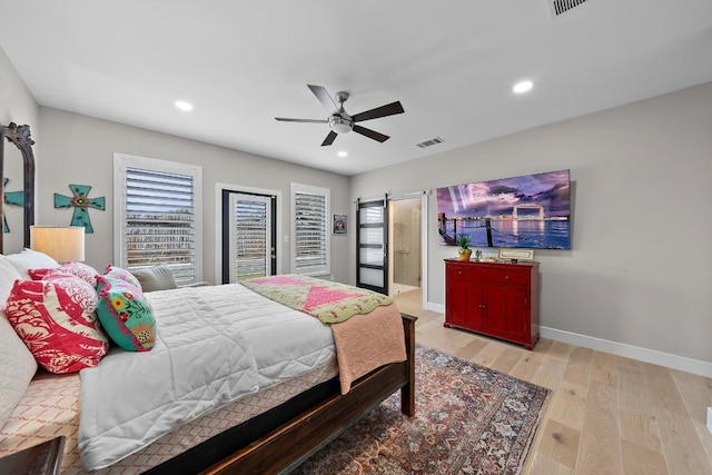 bedroom with a barn door, ceiling fan, and light wood-type flooring