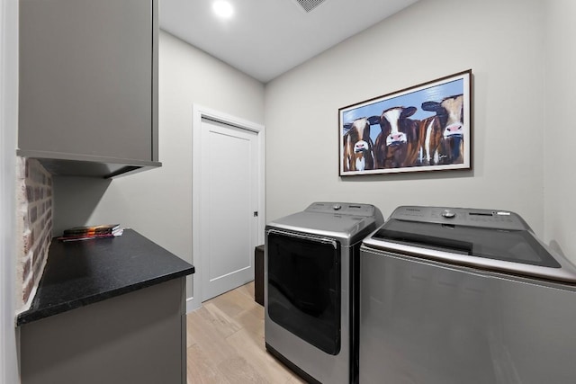 laundry room featuring cabinets, light hardwood / wood-style floors, and washing machine and clothes dryer