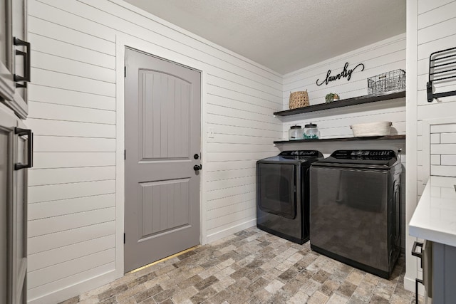 washroom featuring washer and dryer, a textured ceiling, and wooden walls