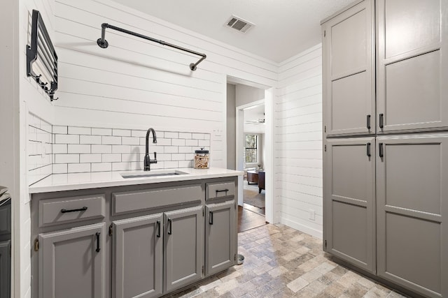 kitchen with backsplash, wood walls, sink, and gray cabinetry