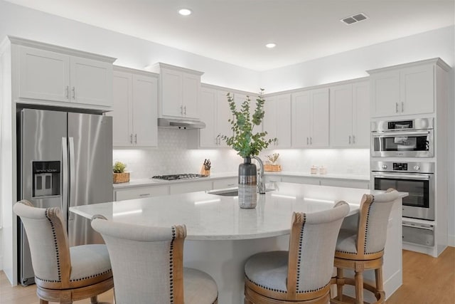 kitchen featuring stainless steel appliances, white cabinetry, a center island with sink, and a kitchen bar