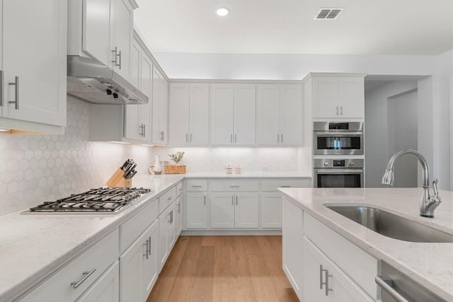 kitchen with stainless steel appliances, white cabinetry, sink, and light stone counters