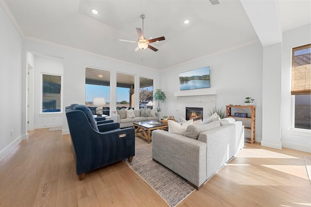 living room featuring a tile fireplace, ornamental molding, ceiling fan, and light hardwood / wood-style floors