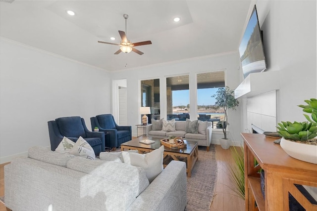 living room featuring hardwood / wood-style flooring, ceiling fan, ornamental molding, and a raised ceiling