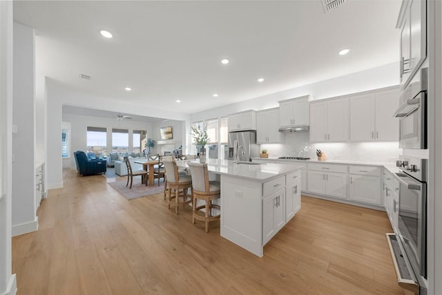 kitchen featuring a breakfast bar, an island with sink, white cabinets, stainless steel appliances, and light wood-type flooring