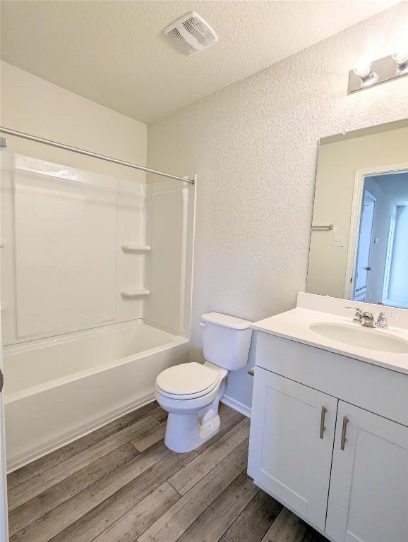 full bathroom with hardwood / wood-style flooring, vanity, toilet, tub / shower combination, and a textured ceiling