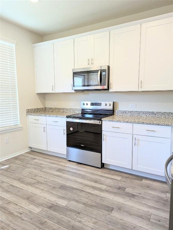 kitchen featuring light stone countertops, light hardwood / wood-style flooring, stainless steel appliances, and white cabinets