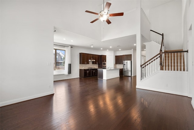 unfurnished living room featuring ceiling fan, dark hardwood / wood-style floors, and a towering ceiling