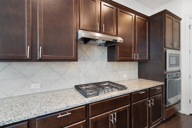 kitchen featuring appliances with stainless steel finishes, dark hardwood / wood-style flooring, decorative backsplash, light stone countertops, and dark brown cabinets