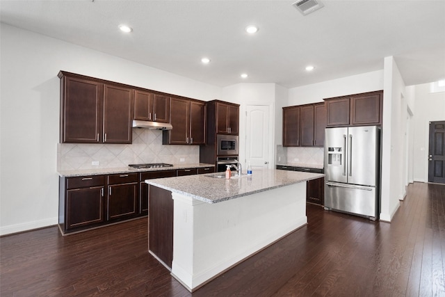 kitchen with sink, dark hardwood / wood-style floors, an island with sink, stainless steel appliances, and light stone countertops