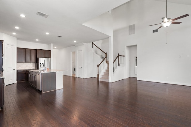 kitchen with ceiling fan, stainless steel refrigerator with ice dispenser, a center island with sink, dark hardwood / wood-style flooring, and decorative backsplash