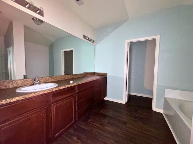 bathroom featuring lofted ceiling, a bathing tub, hardwood / wood-style floors, and vanity