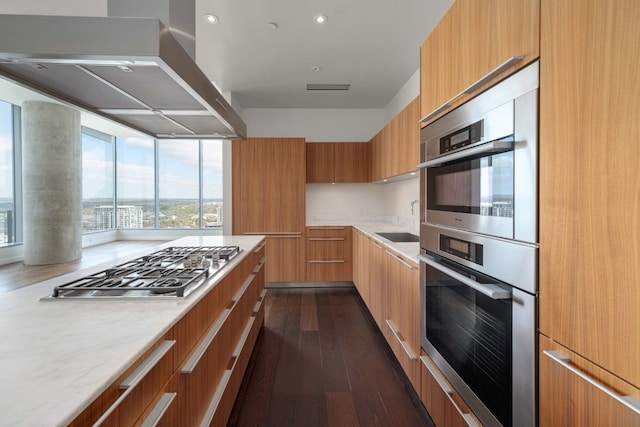 kitchen featuring sink, light stone counters, stainless steel gas cooktop, island exhaust hood, and dark hardwood / wood-style flooring