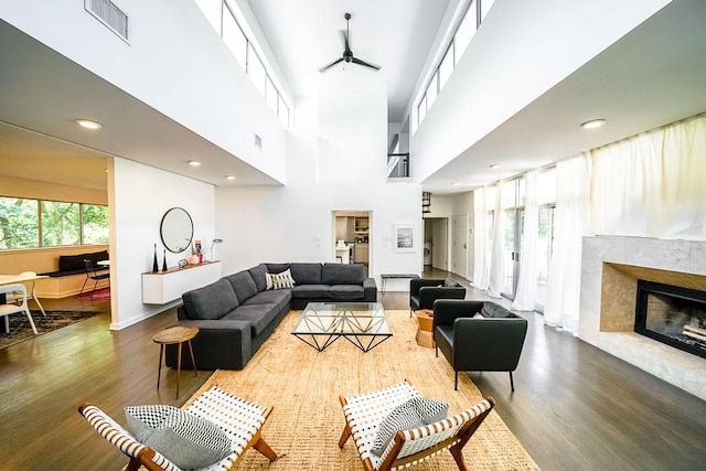 living room featuring a towering ceiling, dark wood-type flooring, a premium fireplace, and ceiling fan