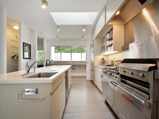 kitchen featuring sink, light hardwood / wood-style flooring, high end appliances, white cabinets, and a center island with sink