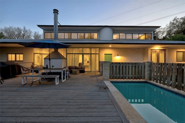 back house at dusk featuring a swimming pool side deck and an outdoor living space with a fire pit