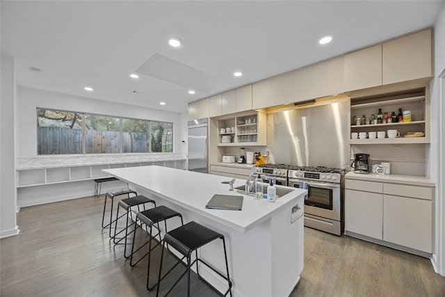 kitchen with a breakfast bar area, appliances with stainless steel finishes, a kitchen island with sink, light hardwood / wood-style floors, and white cabinets