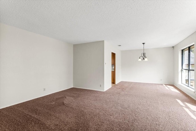 spare room featuring carpet floors, a textured ceiling, and a chandelier