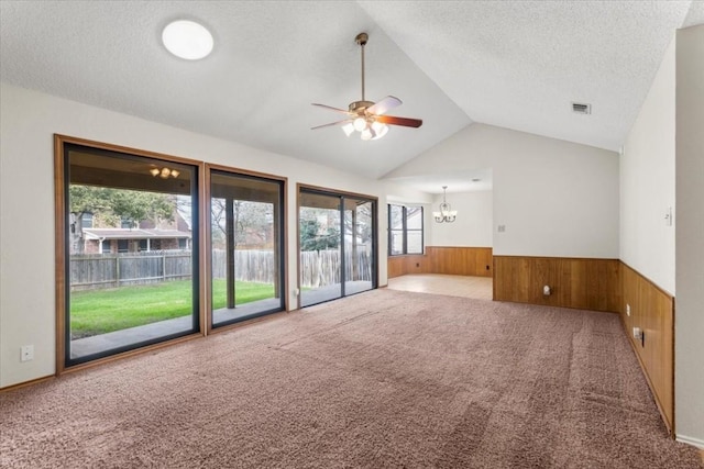 unfurnished living room with vaulted ceiling, ceiling fan with notable chandelier, wooden walls, carpet, and a textured ceiling