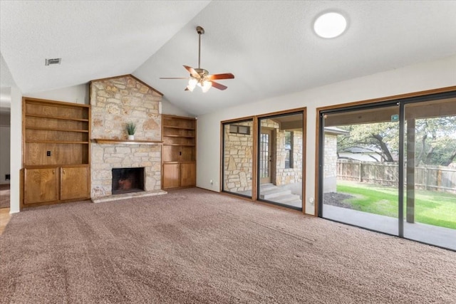 unfurnished living room with built in features, a textured ceiling, a stone fireplace, vaulted ceiling, and light colored carpet