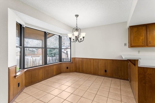 unfurnished dining area with a chandelier, a textured ceiling, wooden walls, and light tile patterned floors