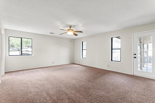 carpeted empty room featuring ceiling fan, plenty of natural light, and a textured ceiling