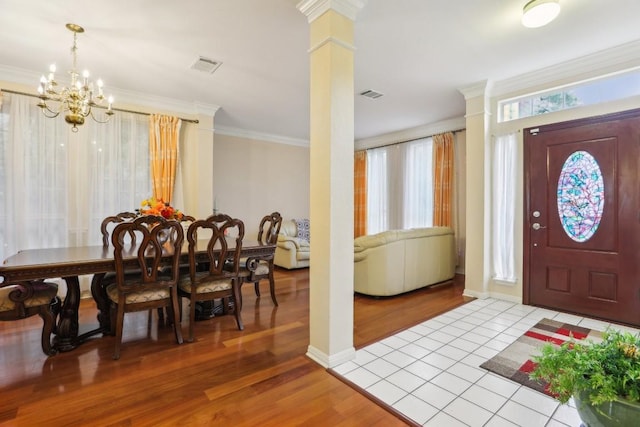 entrance foyer featuring an inviting chandelier, ornamental molding, light wood-type flooring, and ornate columns