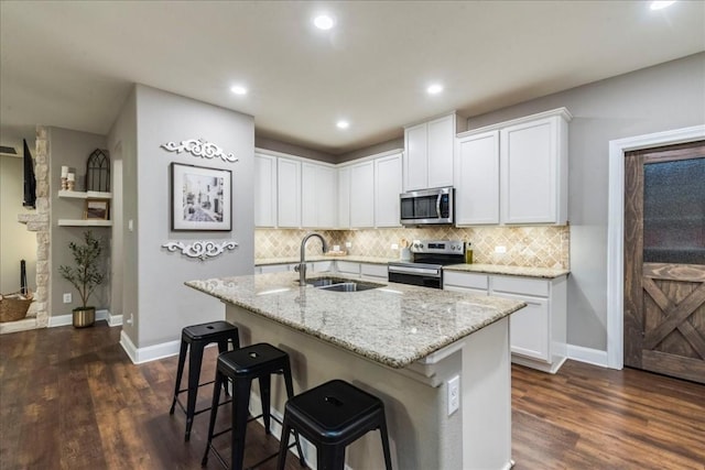 kitchen with a center island with sink, stainless steel appliances, light stone countertops, sink, and white cabinetry