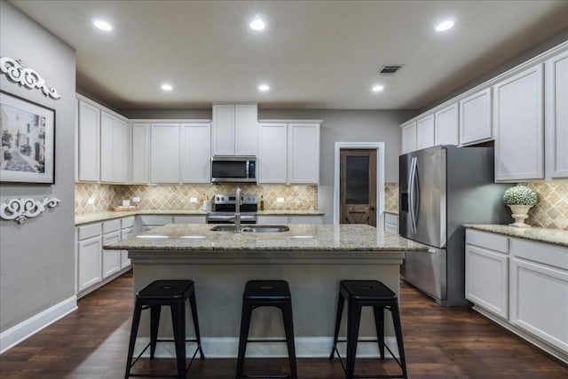 kitchen featuring stainless steel appliances, an island with sink, light stone countertops, white cabinets, and sink