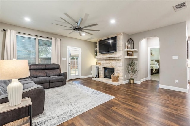 living room with ceiling fan, dark hardwood / wood-style flooring, and a stone fireplace