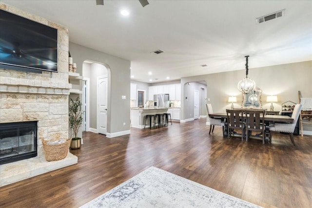 dining area with visible vents, arched walkways, dark wood-type flooring, and a fireplace