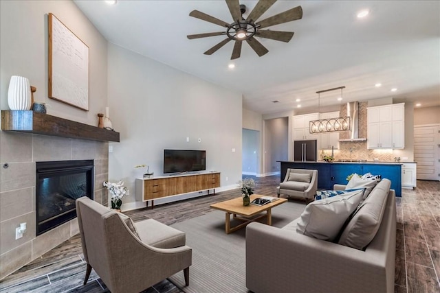 living area with dark wood-style flooring, recessed lighting, a tiled fireplace, a ceiling fan, and baseboards