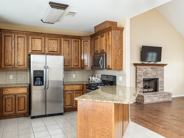 1504 County Road 459, Thorndale, TX 76577 - kitchen with stainless steel appliances, brown cabinetry, a peninsula, light stone countertops, and light tile patterned flooring