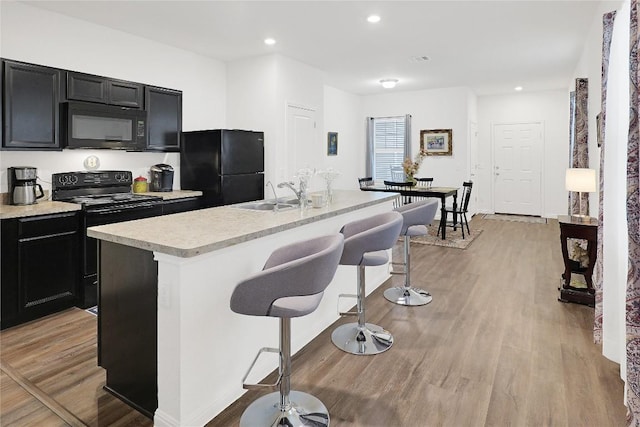 kitchen with sink, a center island with sink, light wood-type flooring, a kitchen breakfast bar, and black appliances