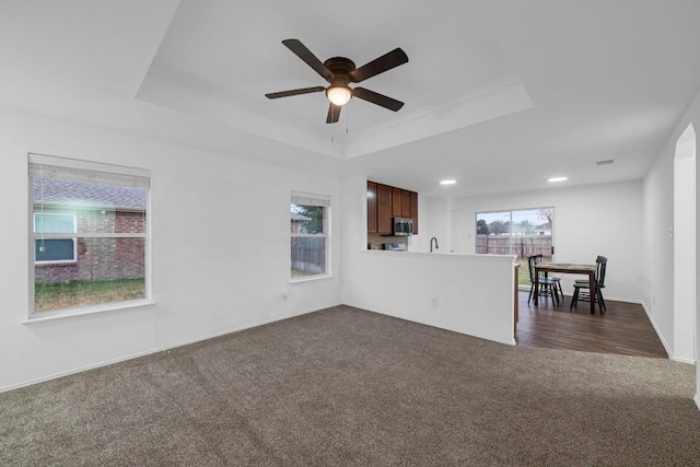 unfurnished living room with dark carpet, a raised ceiling, and a healthy amount of sunlight