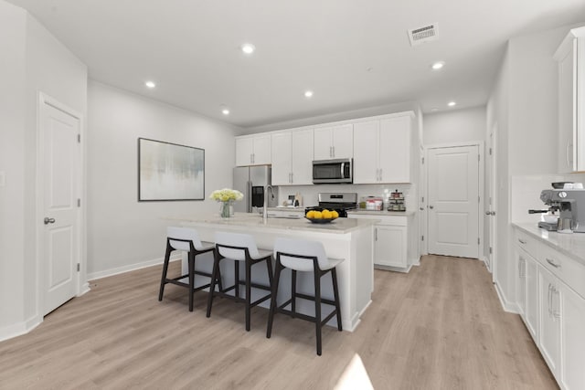 kitchen featuring a breakfast bar, a kitchen island with sink, stainless steel appliances, white cabinets, and light wood-type flooring