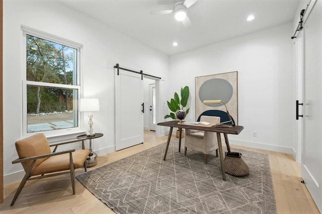 office with ceiling fan, a barn door, and light wood-type flooring