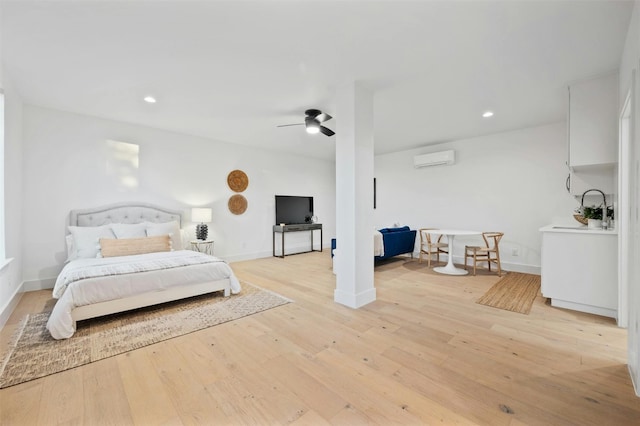 bedroom featuring sink, light hardwood / wood-style floors, an AC wall unit, and ceiling fan